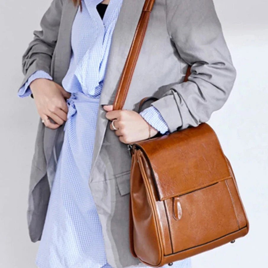 Femme avec chemise bleue rayée et blazer gris portant un sac à dos en cuir de vachette